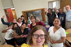 A group of smiling adults waving and holding up the peace sign with their hands.