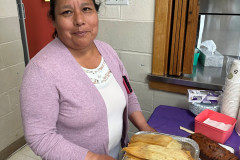 Smiling older adult holding an aluminum pan of delicious homemade tamales.