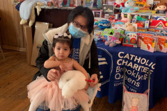 A Catholic Charities volunteer taking a photo with a smiling child in front of a table with baby toys.