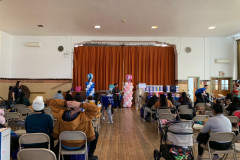 A group of parents seated with children in an auditorium listening to someone speak.