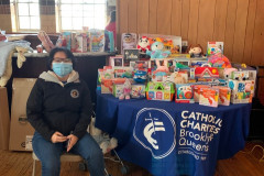 A woman seated in front of a table covered in a blue Catholic Charities table cloth with baby toys on it.
