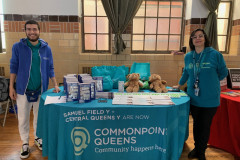 Two smiling individuals posing next to a table  with Commonpoint Queens.