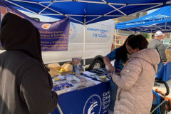 Two people standing under a blue Catholic Charities Brooklyn and Queens tent receiving information and resources about programs and services..