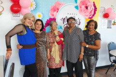 A group of women stand side by side in front of a floral backdrop during a Mother's Day celebration .