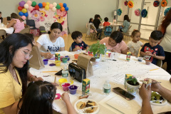Woman and small children are seated at a round table participating in an arts and crafts project.