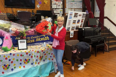 Smiling woman dressed in a red shirt and blue jeans holds up a broken strawberry piñata.