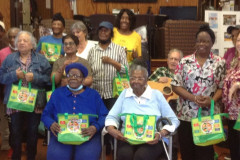 Members of an older adult center are seated holding holding small green tote bags.