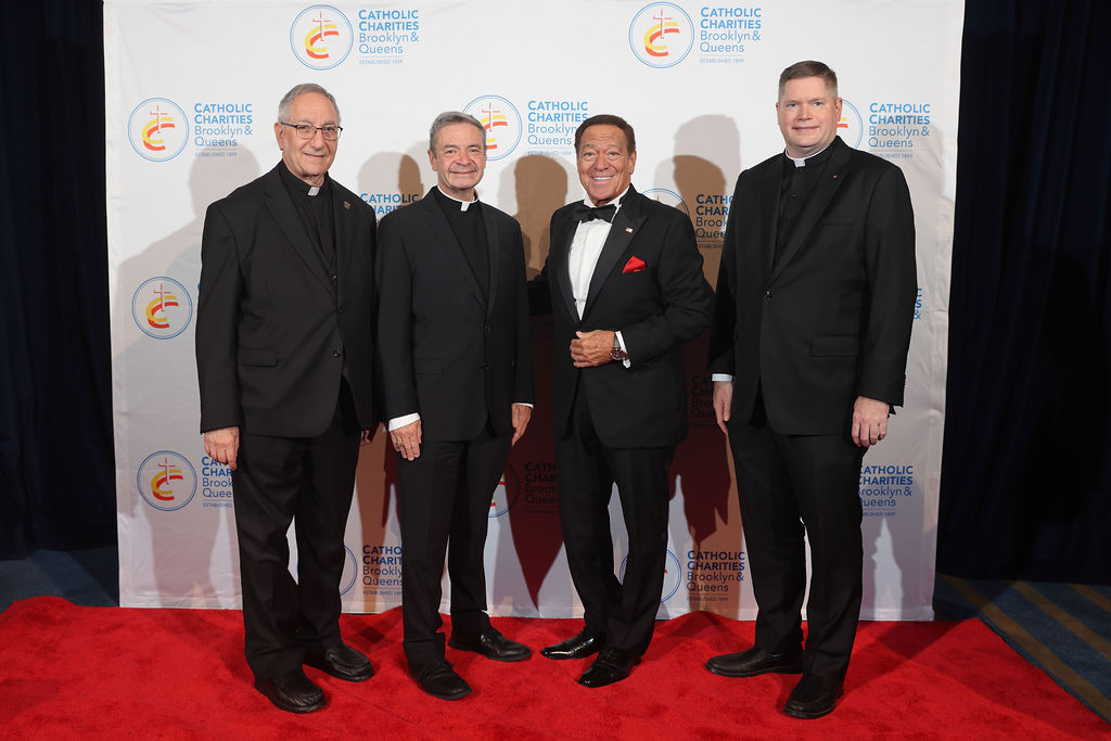Group photo of 4 smiling men dressed in black on a red carpet in front of a step and repeat.